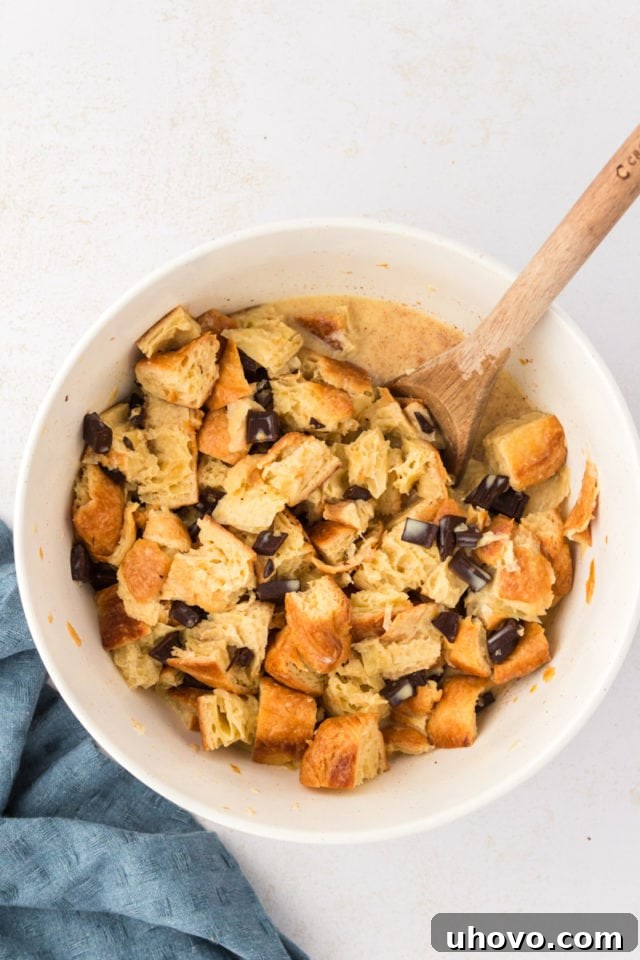 Overhead view of croissants and chocolate pieces mixed in a bowl with the custard