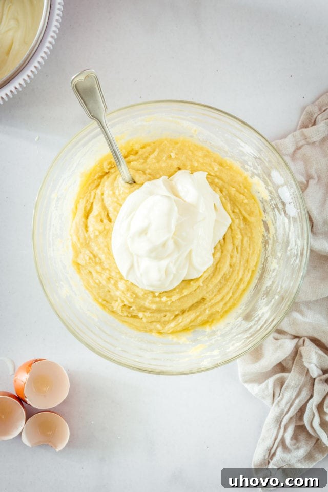 Overhead view of cream cheese being gently folded into the muffin batter in a glass bowl.