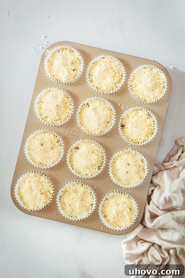 Overhead view of cream cheese muffins in a muffin tin, topped with pecans and ready to be baked.