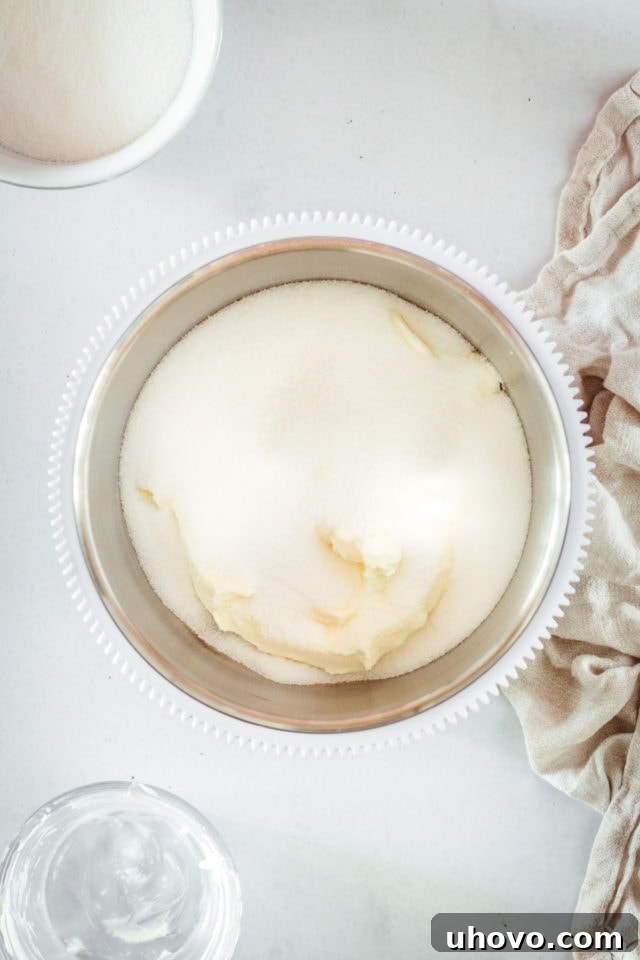 Overhead view of granulated sugar and softened cream cheese in a mixing bowl, ready to be combined.