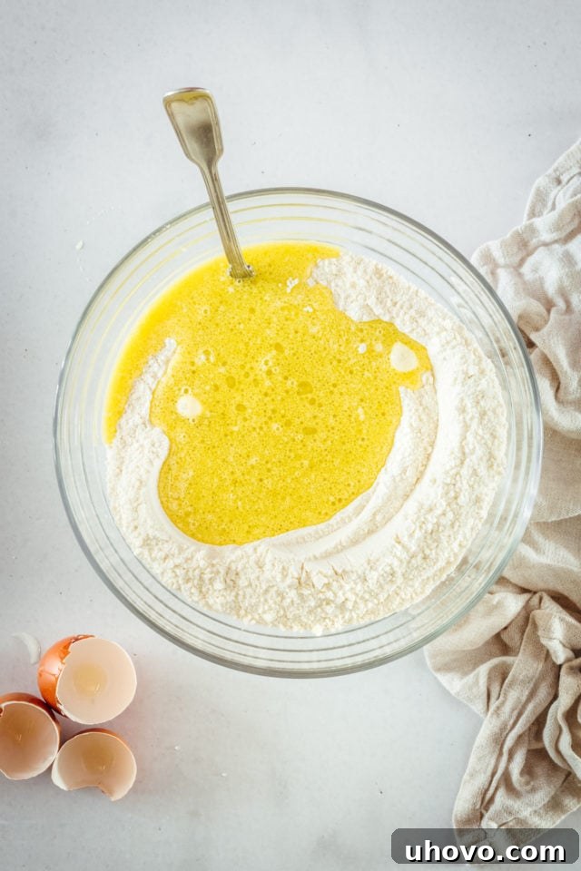 Overhead view of muffin batter being gently mixed in a glass bowl, just until combined.