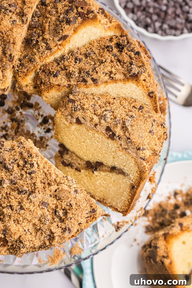 A partially sliced chocolate chip crumb pound cake, showcasing its moist interior and generous crumb layers, gracefully displayed on a clear glass cake stand.