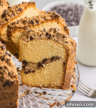 A partially sliced chocolate chip crumb pound cake, beautifully presented on a clear glass cake plate, inviting you to take a bite.