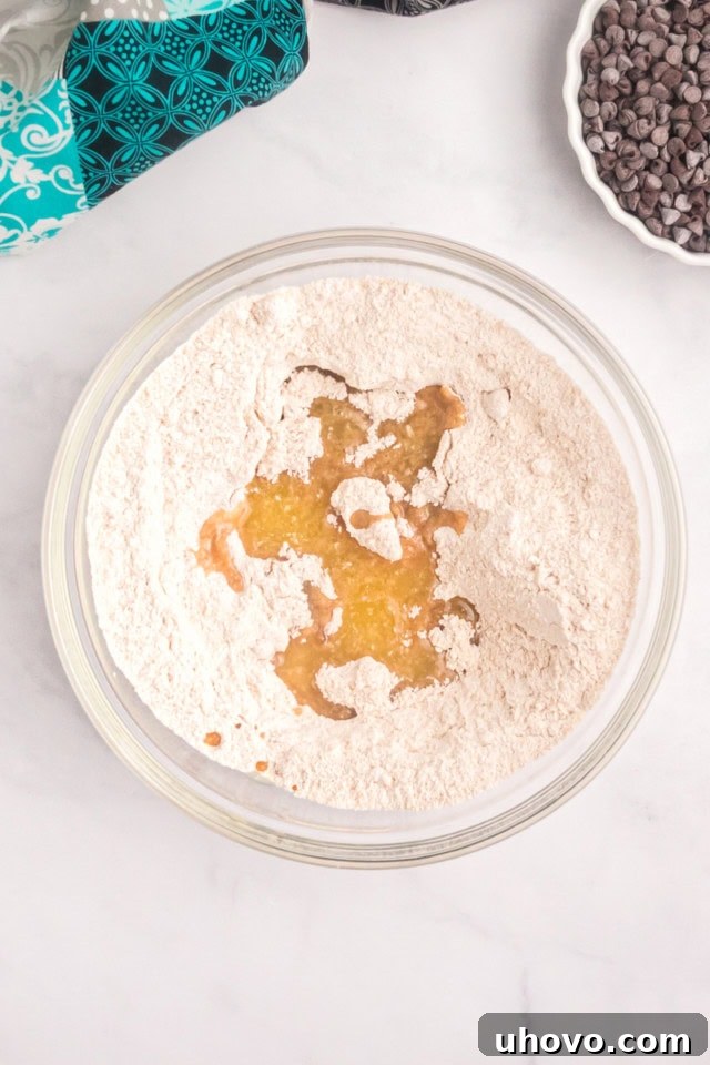 An overhead view of flour, brown sugar, granulated sugar, and cinnamon thoughtfully combined in a clear glass mixing bowl, awaiting the addition of melted butter.