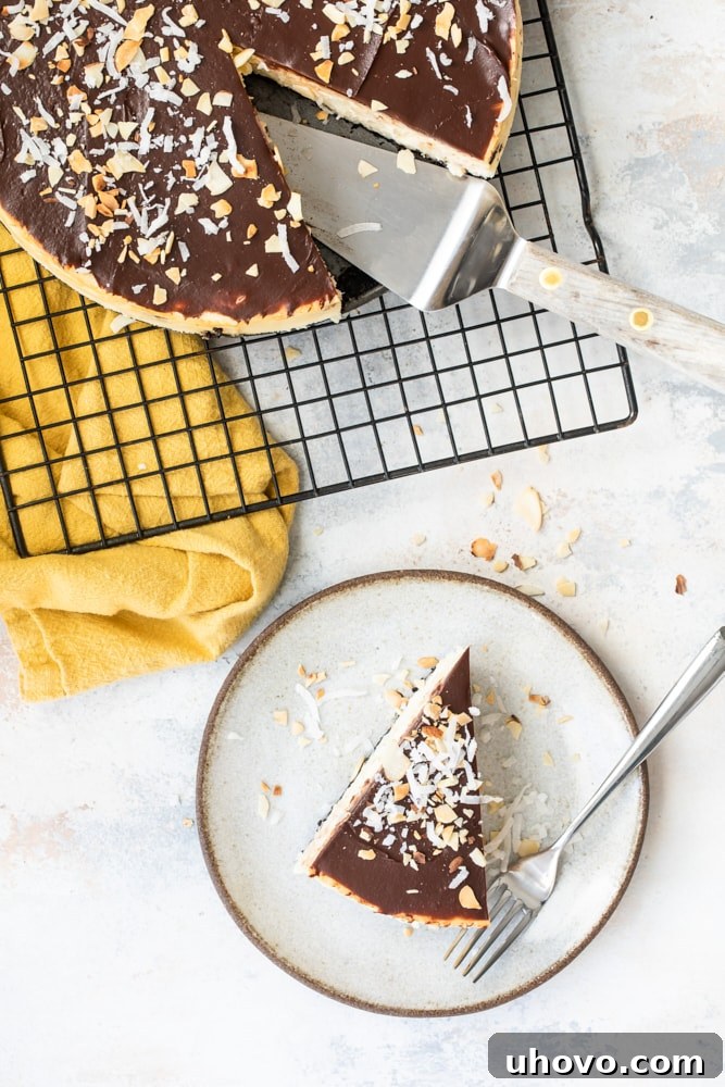An overhead view of a slice of Chocolate Coconut Almond Cheesecake on a beige plate, with the remaining cheesecake cooling on a wire rack in the background.