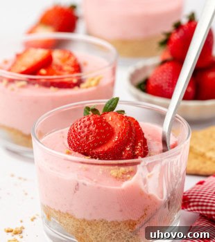 A delightful strawberry no-bake cheesecake with a spoon ready for a bite, more cheesecakes and fresh strawberries partially visible in the background.