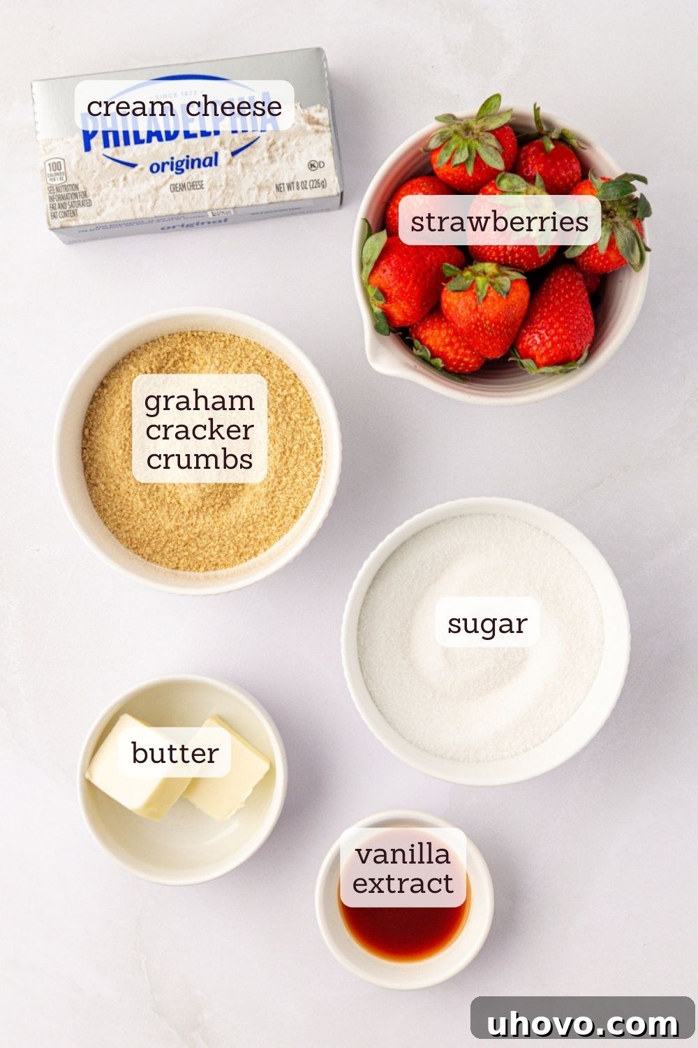 An overhead view showcasing the simple, fresh ingredients required to make strawberry no-bake cheesecakes, including fresh strawberries, cream cheese, graham crackers, and butter.