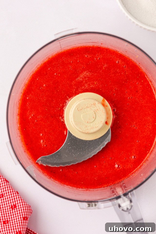 A close-up overhead view of a perfectly smooth, bright red strawberry purée filling the bottom of a food processor bowl after blending.