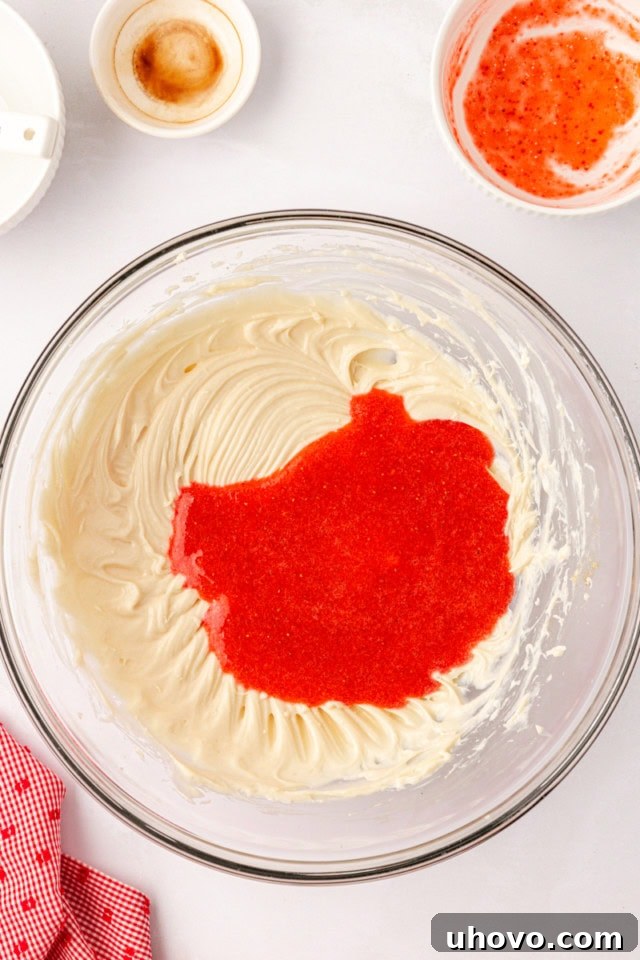 The vibrant strawberry purée being poured into a mixing bowl containing the whipped cream cheese, sugar, and vanilla mixture, preparing to be blended.