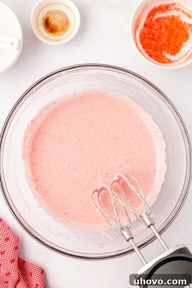 A close-up overhead view of the smooth, pale pink strawberry no-bake cheesecake filling in a glass mixing bowl, perfectly blended and ready for assembly.