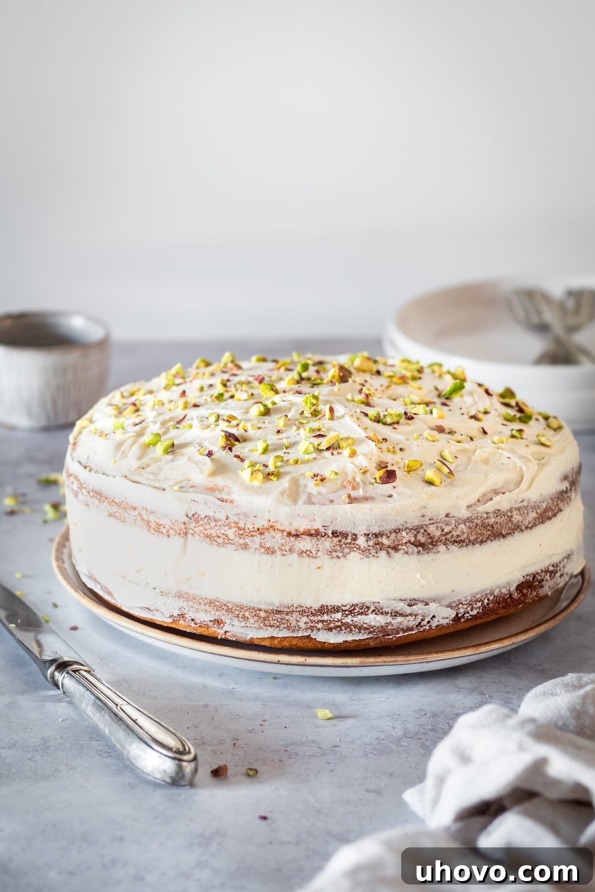 Whole Pistachio Cake pictured with knife, small bowl, plates, and forks, ready for serving.