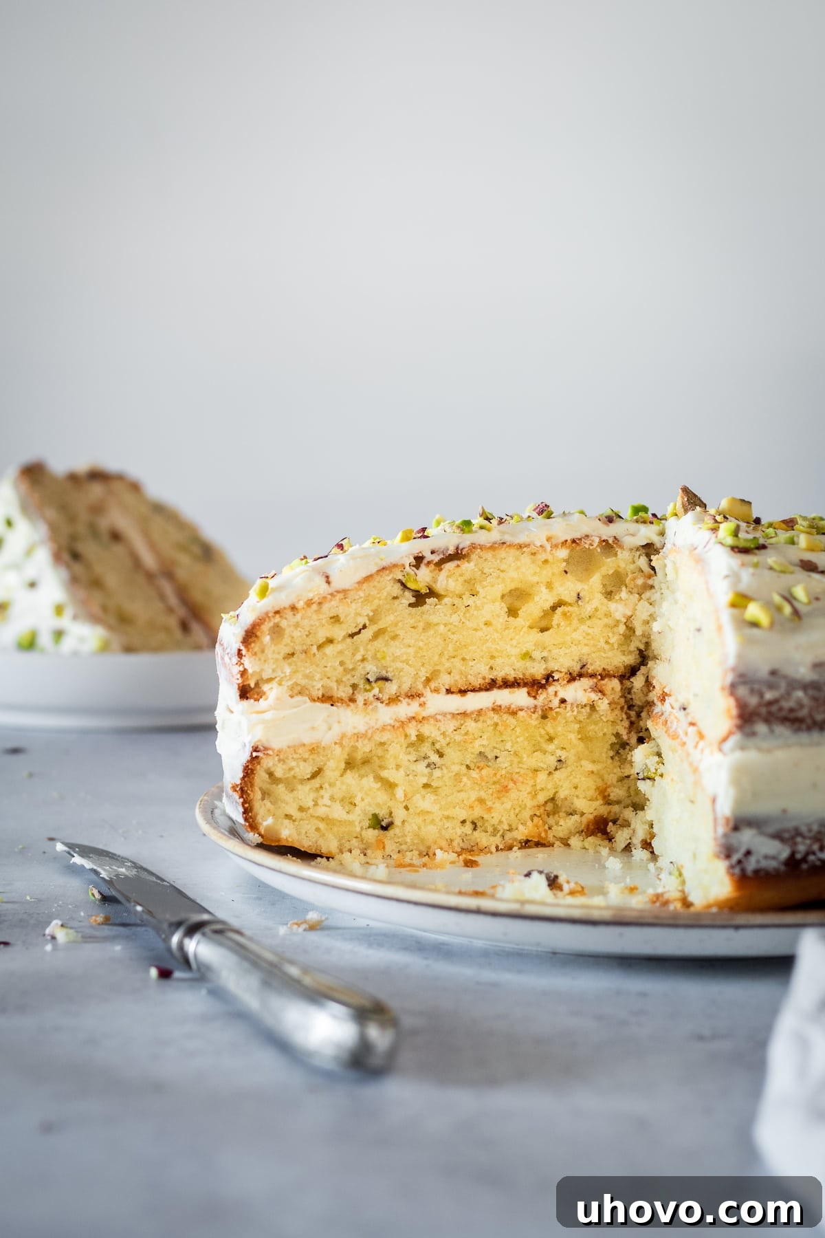 Pistachio Cake on a cake stand with two slices already removed, showing the moist layers and frosting.