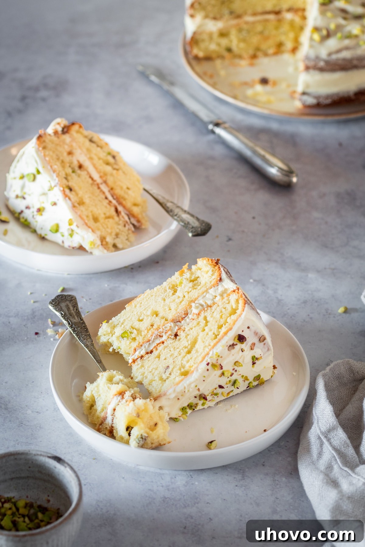 Two perfect slices of Pistachio Cake, beautifully frosted, presented on white plates.