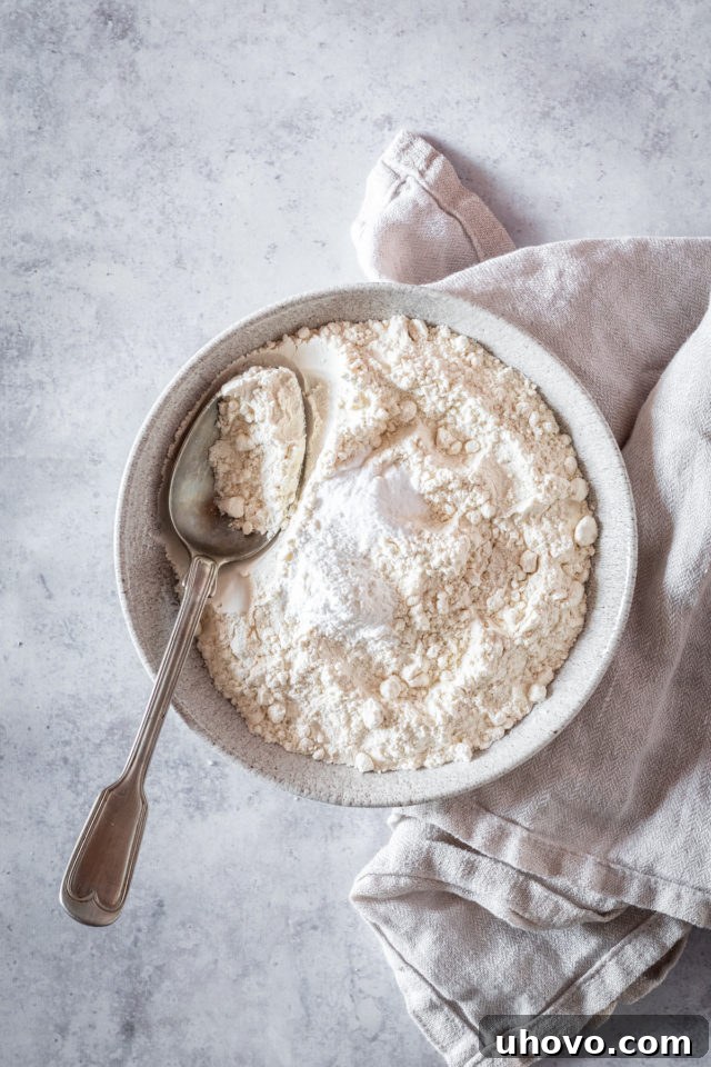 Overhead shot of dry cake ingredients (flour, baking powder, baking soda, salt) in a large white bowl with a whisk.