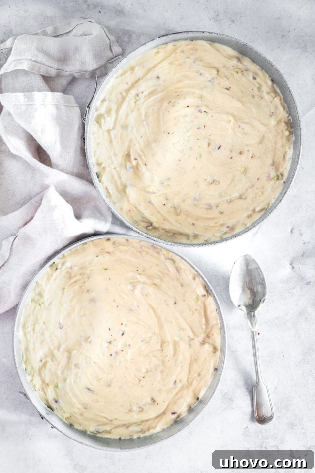 Overhead shot of smooth pistachio cake batter evenly divided into two round cake pans, ready for baking.
