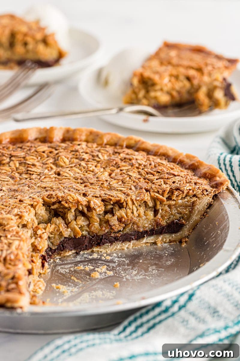 A black bottom oatmeal pie with two slices removed, showing the rich chocolate layer. Slices are visible on plates in the background.