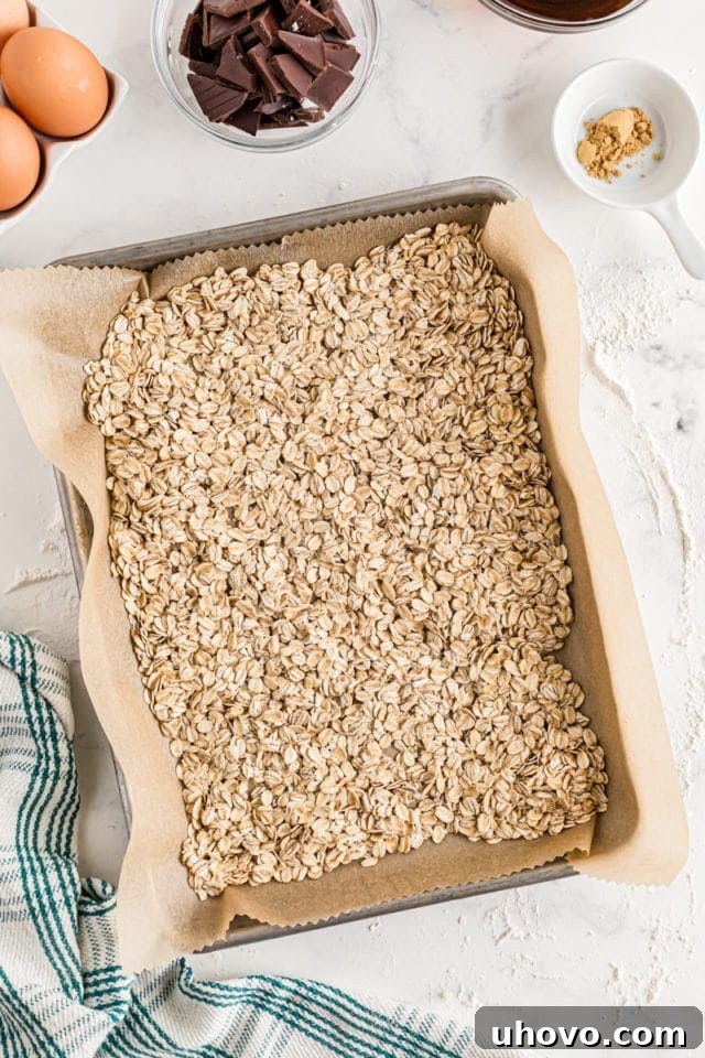 Old-fashioned rolled oats spread evenly on a parchment-lined baking sheet, ready for toasting.