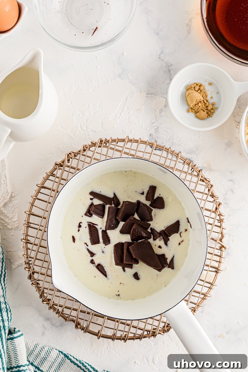 Roughly chopped bittersweet chocolate pieces immersed in hot heavy cream in a saucepan, beginning the ganache process.