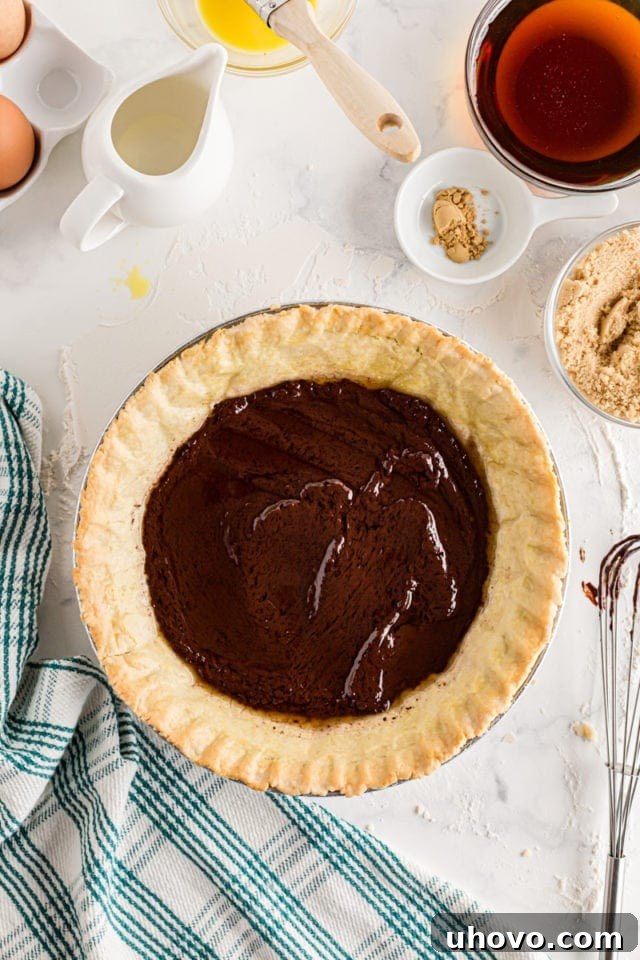 A perfectly smooth layer of chocolate ganache spread evenly over the bottom of a par-baked pie crust.