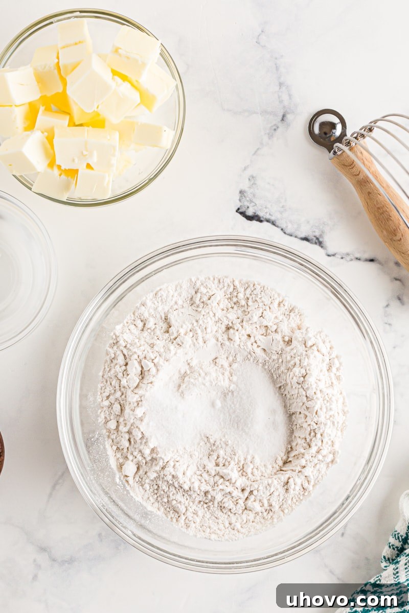 A bowl of all-purpose flour sits beside a bowl of cold, diced unsalted butter, ready for making pie crust.