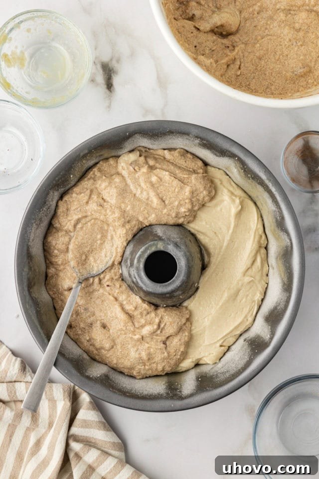 The spiced cinnamon batter being carefully spooned over the plain batter in the Bundt pan