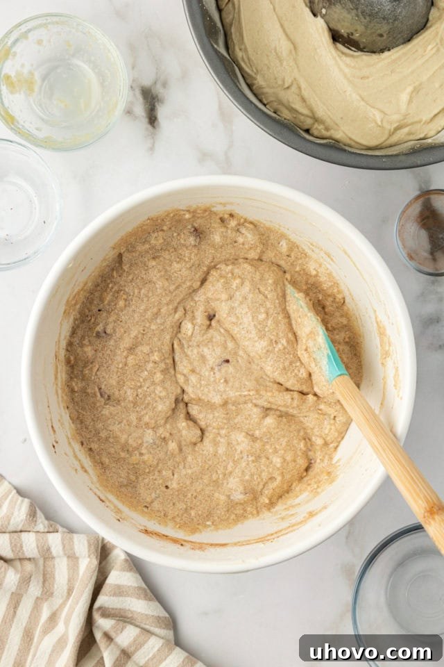 Cinnamon oat cake batter with nuts and applesauce stirred in, in a mixing bowl