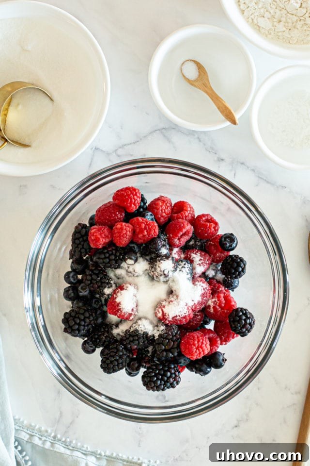 An overhead view capturing the vibrant colors of fresh berries nestled with granulated sugar in a clear glass mixing bowl, just before combining.