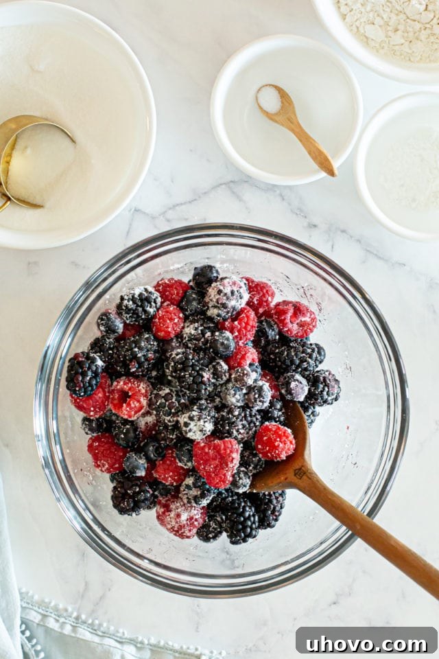 A second overhead view showing the same berries and sugar, now gently mixed together in the glass bowl, sparkling with sweetness.