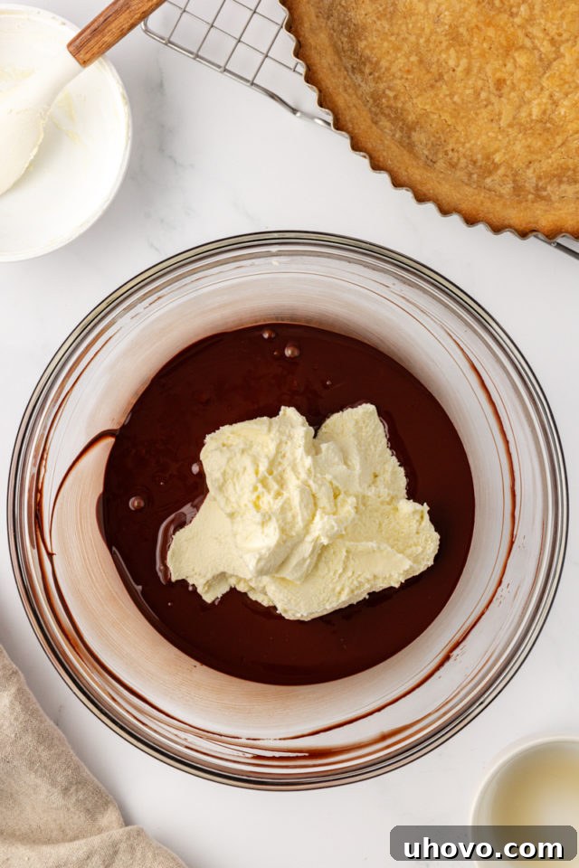 Softened mascarpone cheese and hazelnut liqueur being added to the cooled melted chocolate in a glass mixing bowl.