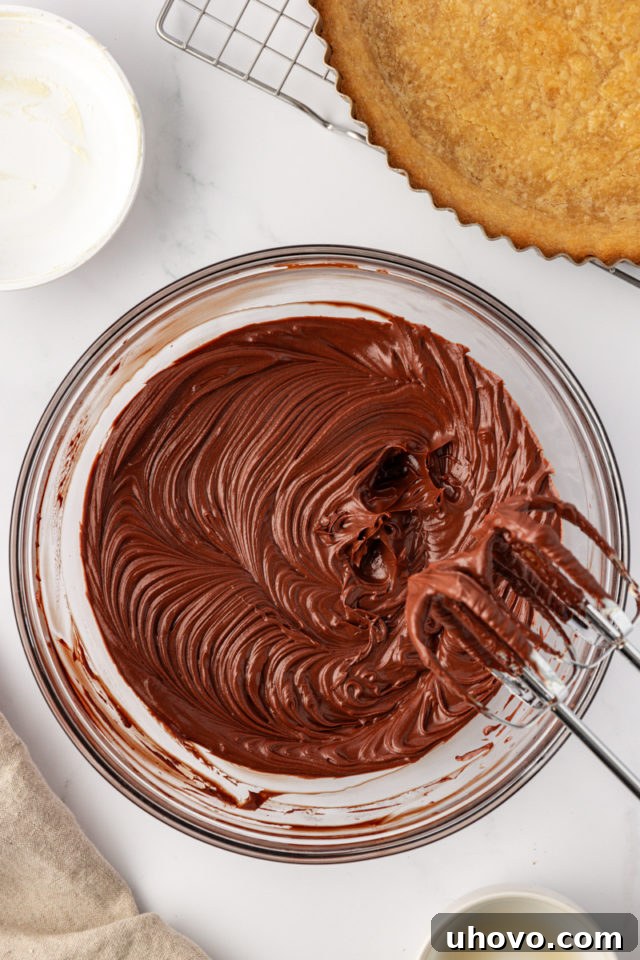 A bowl of creamy, smooth chocolate mascarpone tart filling, rich and glossy, ready to be spread into the baked crust.