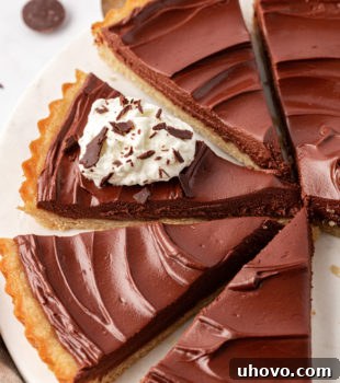 A beautifully presented, partially sliced chocolate mascarpone tart on a white cake plate, with a rich, dark filling.