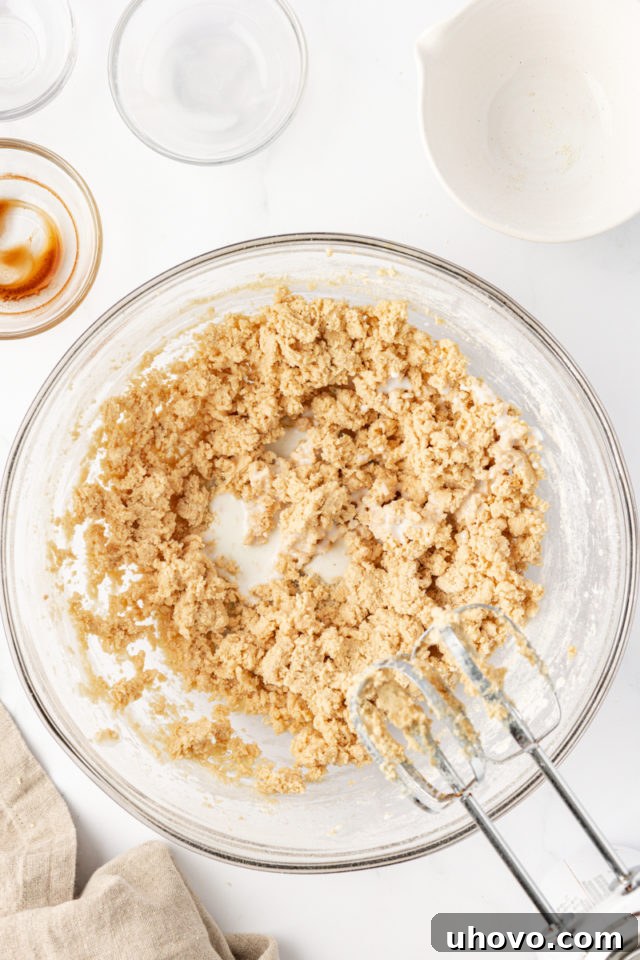 A small amount of milk being gently poured into the tart crust dough mixture in a glass bowl to bring it together.