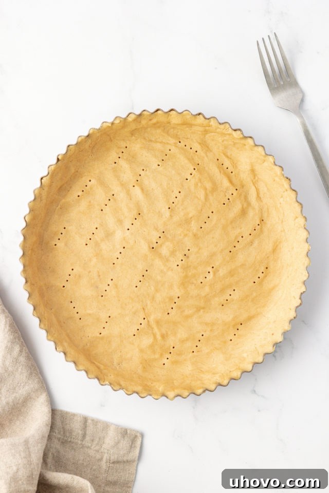 Tart crust dough expertly pressed into a 9-inch tart pan with a removable bottom, with a fork used to prick holes to prevent puffing during baking.