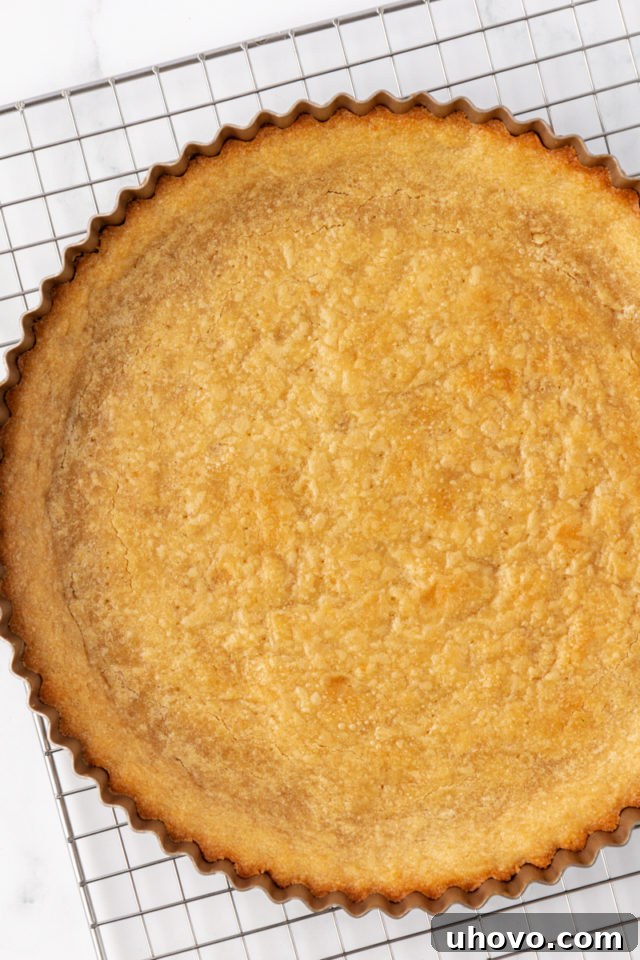 A freshly baked tart crust, golden brown and perfectly set, cooling on a wire rack after being removed from the oven.