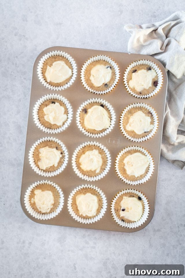 Overhead view of cream cheese filling being carefully added to muffin batter in a tin.