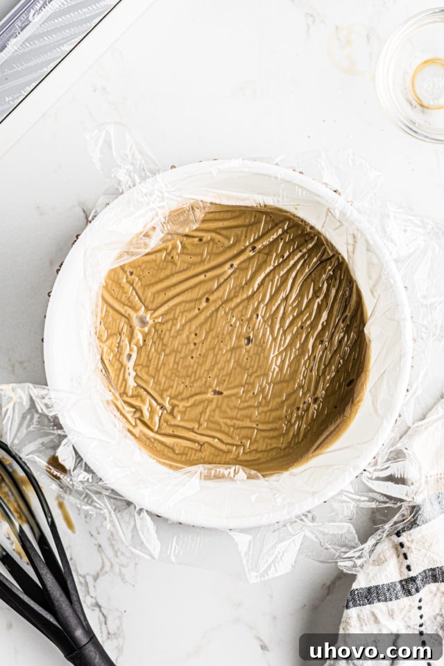 Butterscotch pudding in a bowl, meticulously covered with plastic wrap pressed directly onto its surface to prevent a skin from forming.