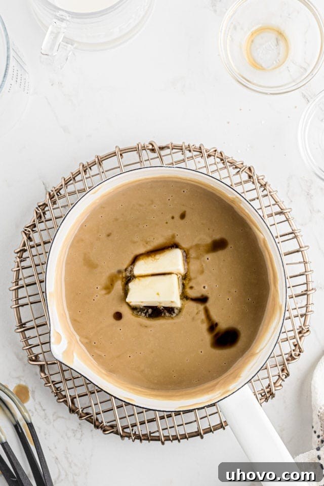 Vanilla extract and cubed butter are added to the warm butterscotch pudding in the saucepan, infusing it with flavor and richness.