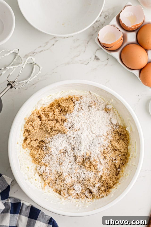Adding brown sugar and all-purpose flour to the beaten cream cheese in a mixing bowl.