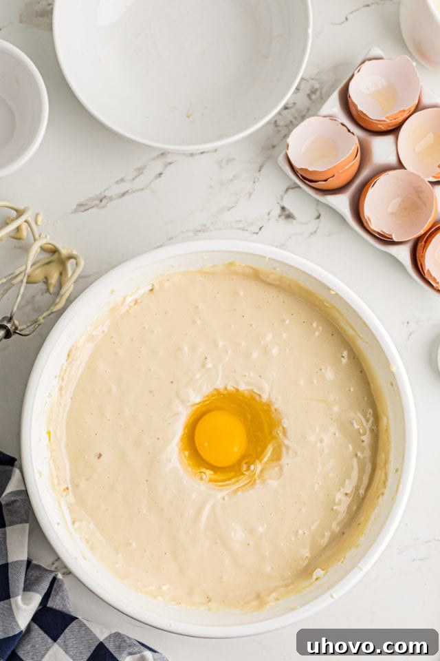 Adding large room-temperature eggs one by one to the cheesecake batter in a stand mixer, ensuring each is fully incorporated.