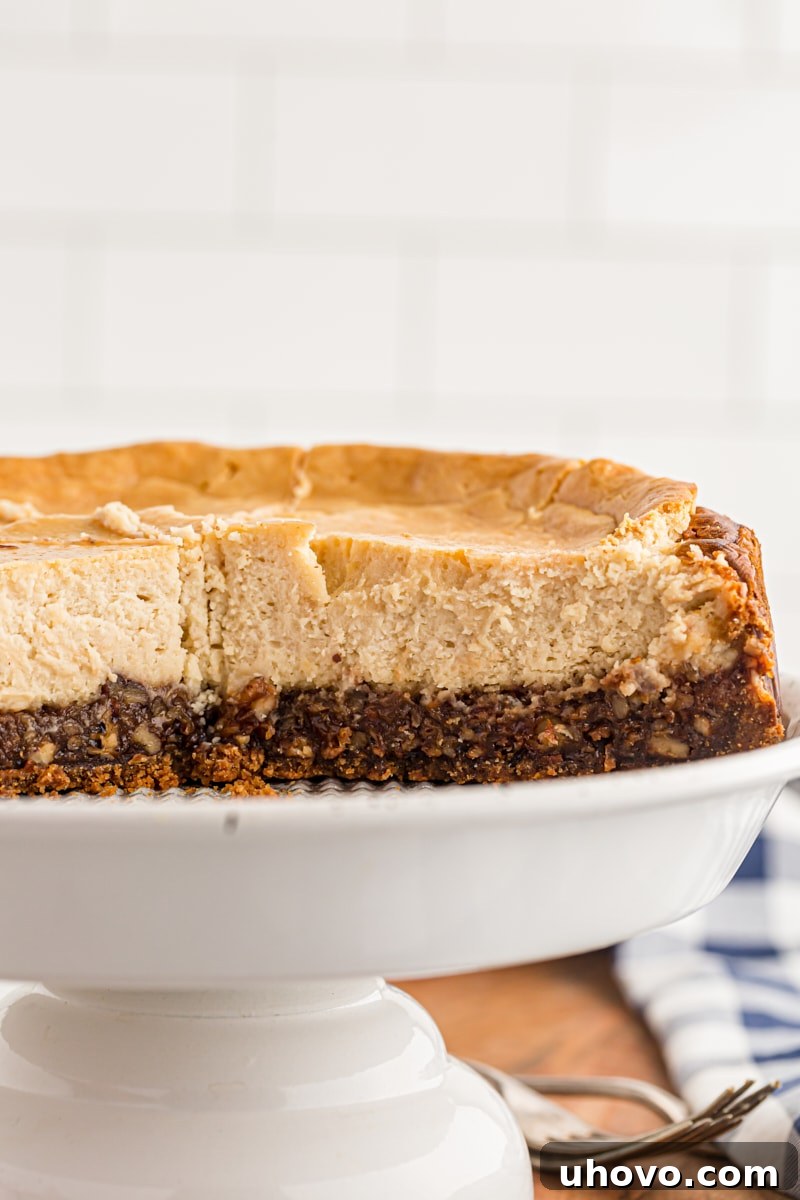 A whole pecan cheesecake with several slices already removed, showing the golden-brown crust, rich pecan filling, and creamy white cheesecake layer.