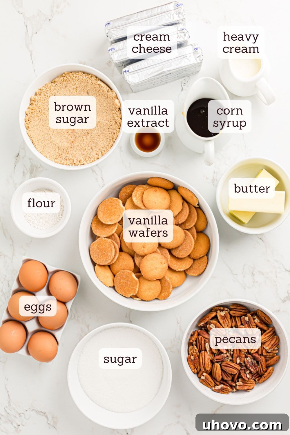 An overhead view of all the fresh ingredients laid out, ready for making the pecan pie cheesecake, including vanilla wafers, pecans, cream cheese, and eggs.