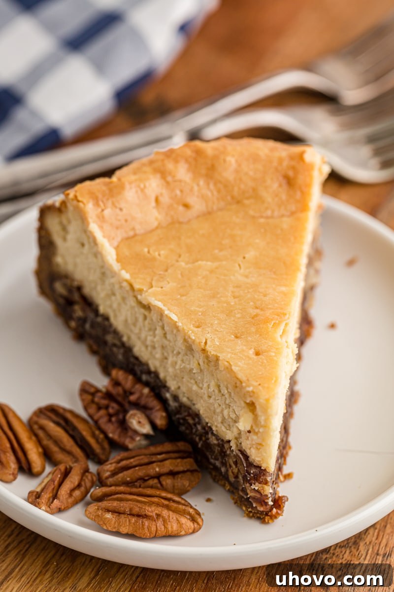 A perfect slice of Pecan Pie Cheesecake with a fork on a white plate, highlighting its distinct crust, pecan, and cheesecake layers.