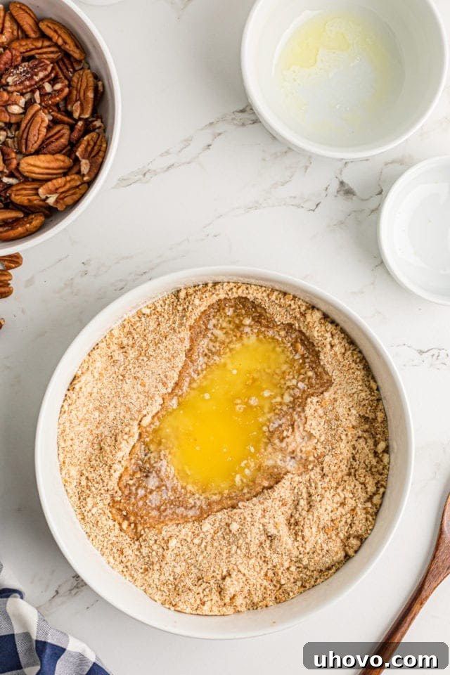 Adding melted butter to the crushed vanilla wafer and brown sugar mixture in a bowl, preparing for the cheesecake crust.
