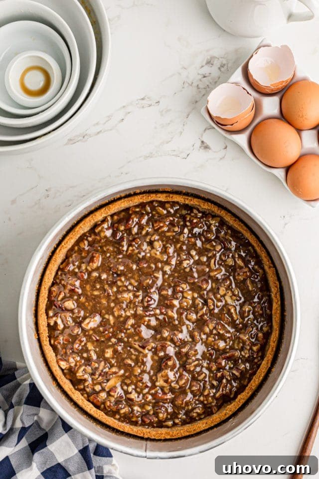 Pouring the warm, thickened pecan pie filling evenly over the pre-baked vanilla wafer crust in a springform pan.