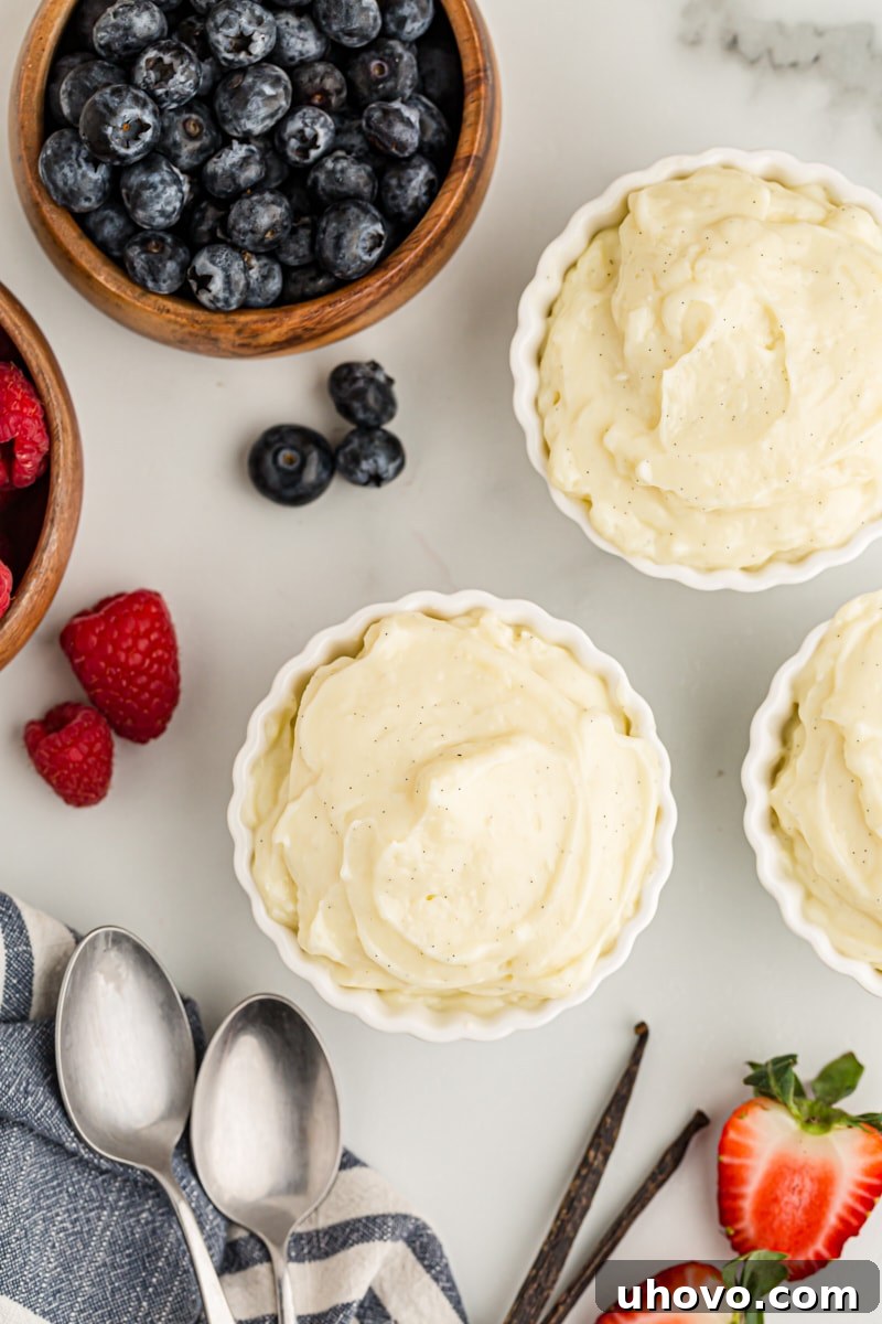 Overhead view of three small custard cups filled with homemade vanilla pudding, artfully arranged with fresh, vibrant berries, creating an inviting and healthy dessert option.