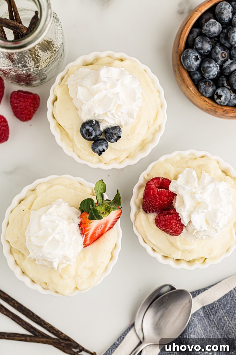 Overhead view of three elegant cups of vanilla pudding, each beautifully garnished with fluffy whipped cream and a medley of fresh berries, ready for serving.