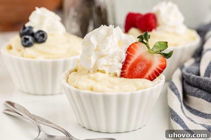 Three cups of homemade vanilla pudding topped with fresh whipped cream and a mix of vibrant berries, beautifully presented for a delightful dessert.