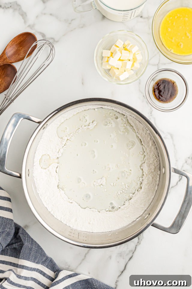Overhead view of milk being carefully added to a mixture of dry ingredients in a saucepan, the first step in creating smooth vanilla pudding.