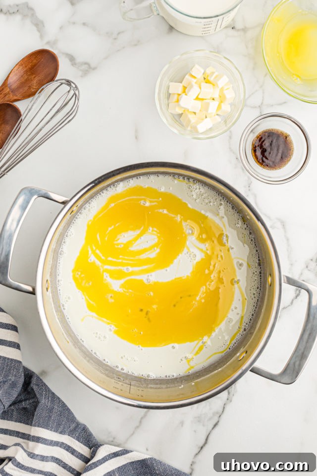 Overhead view of bright yellow egg yolks being gently whisked into the pudding mixture in a saucepan, adding richness and color.