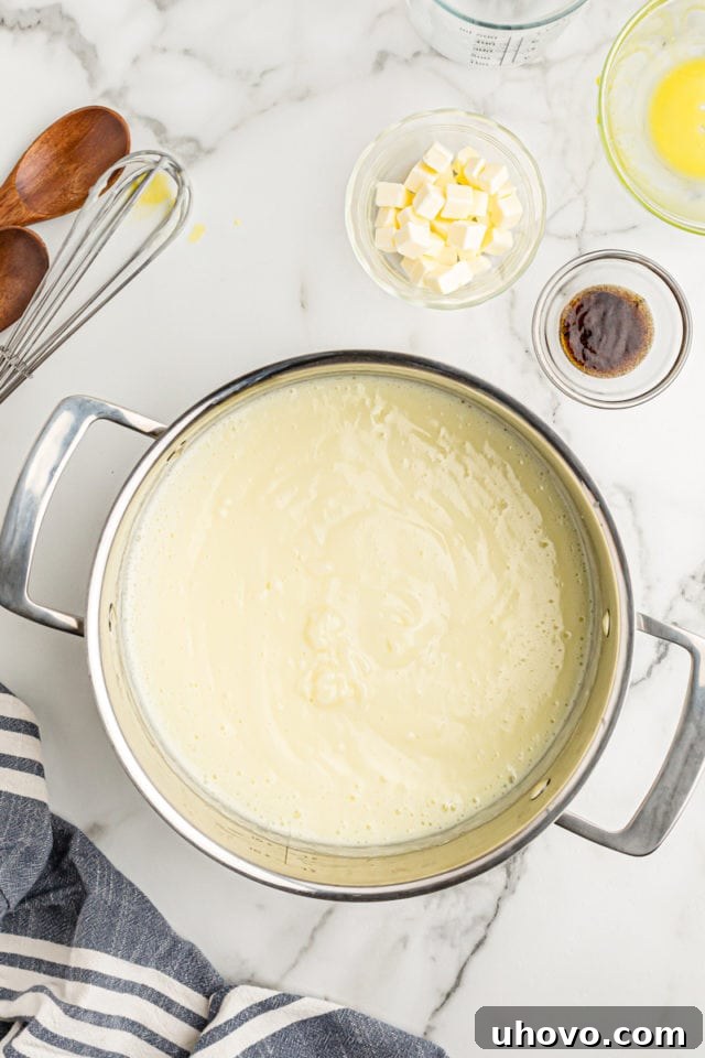 Overhead view of the vanilla pudding mixture in a pan, with small bowls of butter and vanilla extract ready to be incorporated, signaling the next stage of cooking.